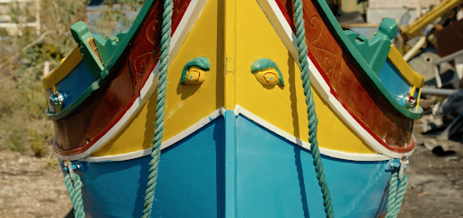 The front of a fishing boat docked on the beach, with bright hues of blue and yellow. Aqua-coloured ropes can also be seen hanging from it.
