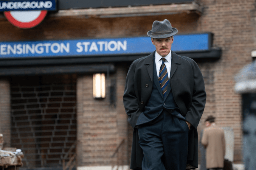 Benedict Cumberbatch walks away from Kensington Station in a slightly baggy three-piece suit and brimmed hat.