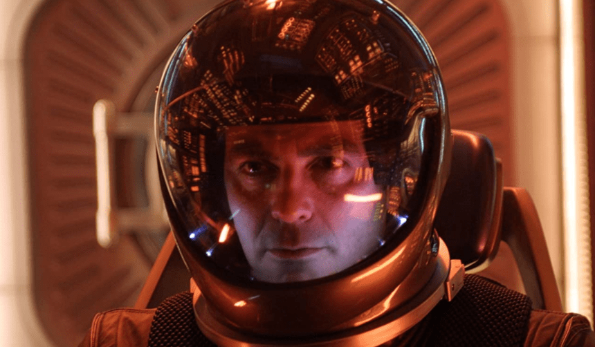 George Clooney in a space suit; the glass of the suit reflects a vast control room.