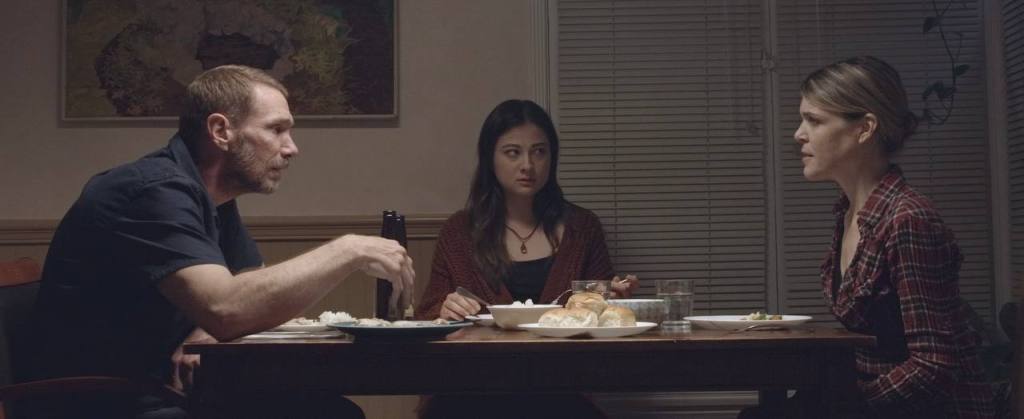 Edward Wooden as Rick, Nicole Ohara as Elyse, and Juls Hoover as Sheila are seated at a rectangular dinner table. Rick and Sheila are seated on opposite ends of each other while Elyse is positioned in the middle of them, along the horizontal edge.