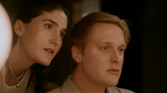 Still from the self-referential scene that takes place backstage. It captures Berlant and Early from the reflection of a mirror in their lounge. The lightning is warm and soft. Early looks teary-eyed and composed in his appearance as he looks straight ahead directly at himself. Behind him, leaning into him, is Berlant. She looks with wide open eyes at his reflection, as if she's caught in a moment of trying to either encourage or persuade him - and, either way, she is clearly the one in control of the moment. 