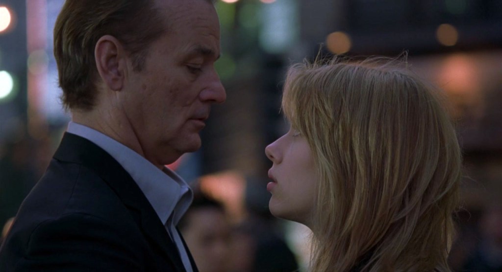 A still of Bill Murray as Bob and Scarlett Johansson as Charlotte in 'Lost in Translation'. They stand in profile view, facing one another.
