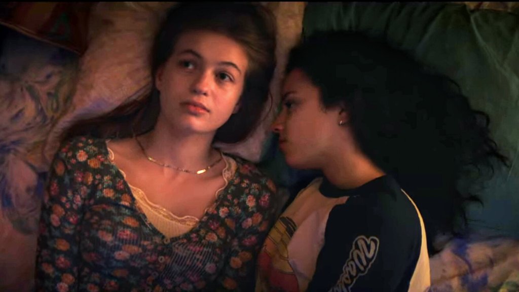 A still from 'Fear Street Part 1: 1994'. Sam (Olivia Scott Welch) lays on a bed and glances away, with Deena (Kiana Madeira) laying next to her on her side.