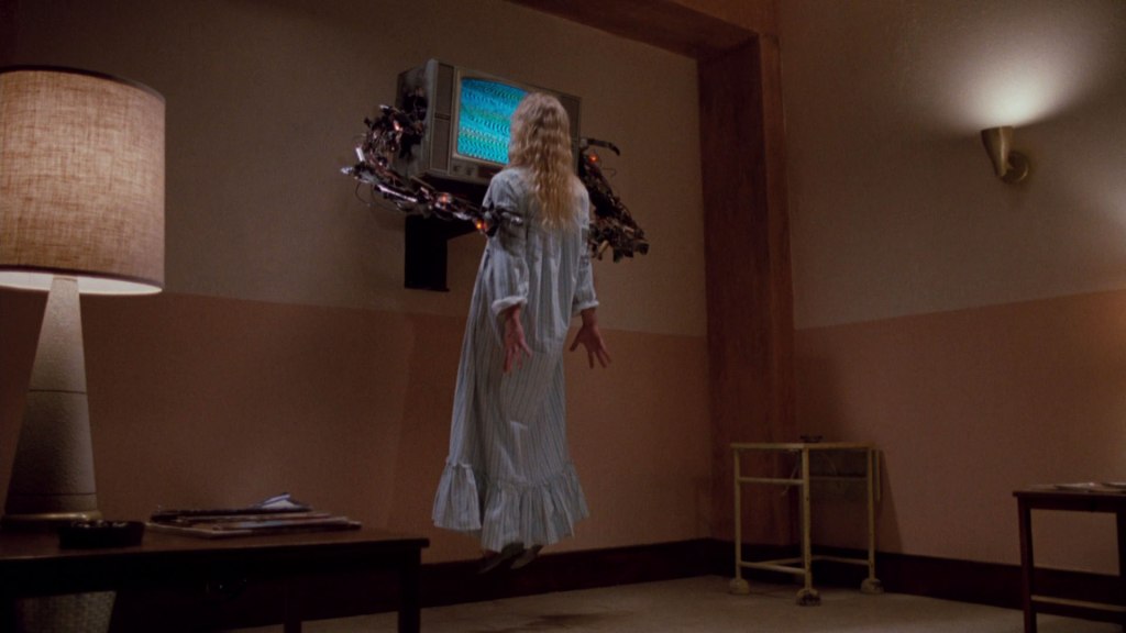 Jennifer being lifted off the ground by robotic arms towards the television set