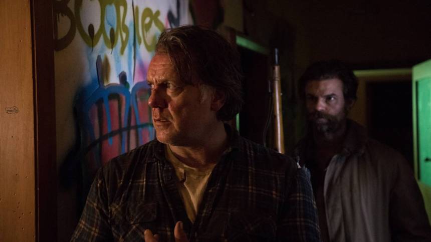 Still portraying Hoaggie in the front with Mandrake close behind, looking at him while holding his gun. Mandrake looks determined and black in his eyes, Hoaggie – who is looking around him as memories come back – looks uncomfortable. They are at the boys' home, behind them walls are seen covered with graffiti. 