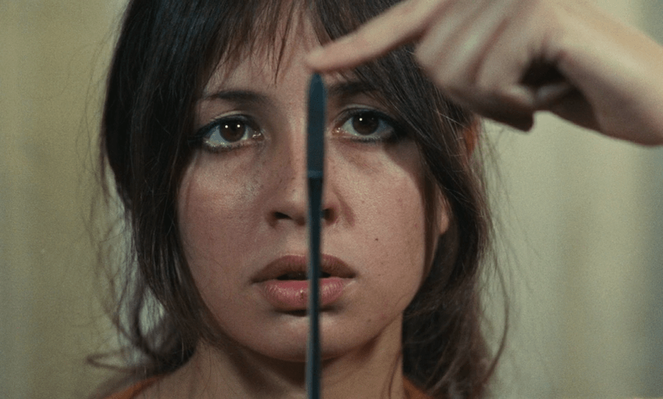 A still from Juliet in Paris showing the female protagonist in a close-up looking at a thin surgical knife she's holding. She has a finger on its pointy tip, as to see how sharp it is. 