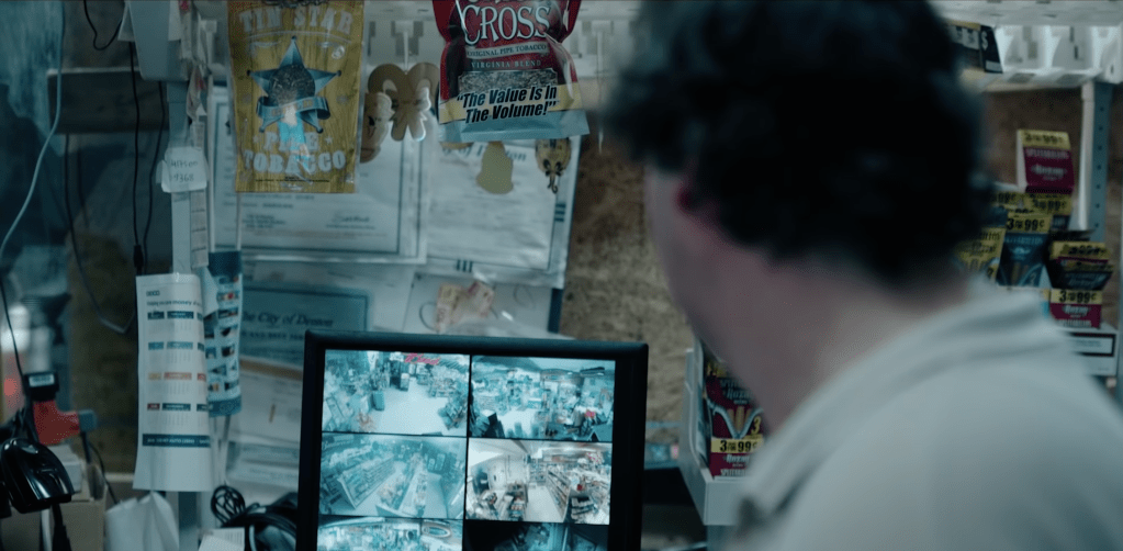 Still from Monitor showing the protagonist out of focus with his head turned away from the viewer as he's looking at his security camera monitors. 