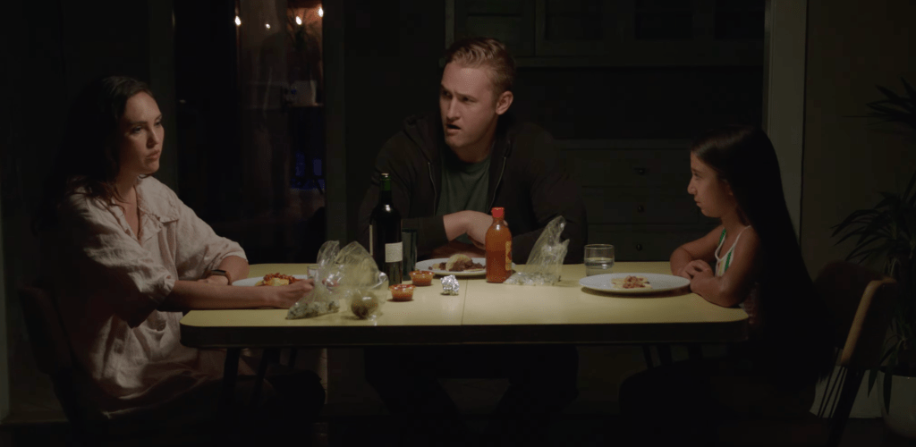 Still from Place showing the protagonists - the family - sitting at a table having dinner. The boyfriend and daughter are both looking at the woman to the left as she's talking.
