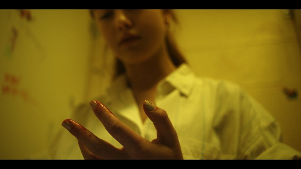 Still from The Boogeywoman showing the female protagonist looking at her bloody fingers in a bathroom stall. 