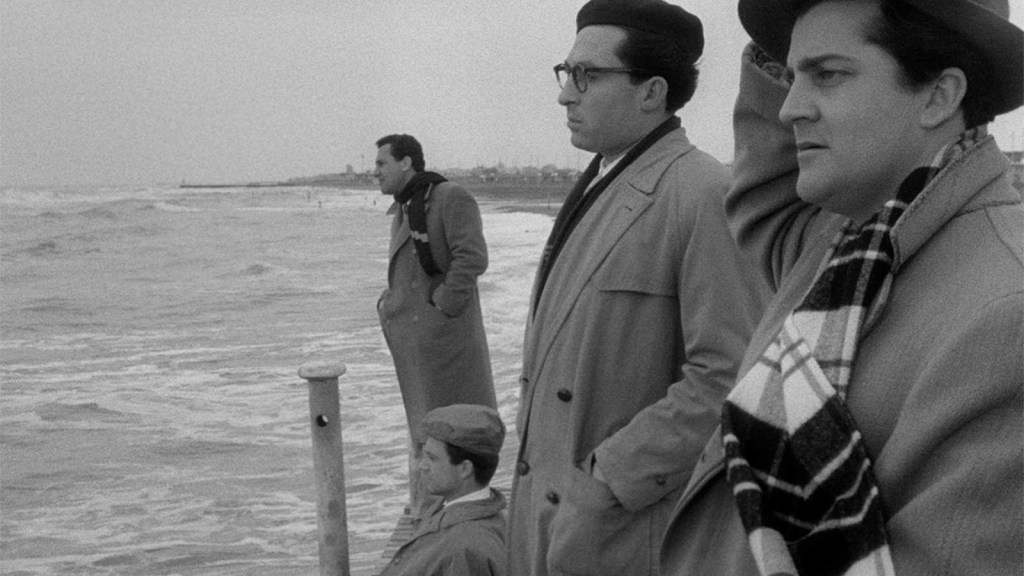 Showing four of the five friends in profile, all but Moraldo standing up (he is sitting down on the dock) whilst looking out towards the open sea. They all look deep in thought, not speaking to each other. It's a windy day, as one of them is holding onto their hat. 