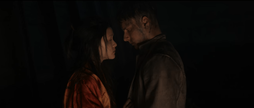 Ling Yi and Olek caught in a moment of romance amongst the threatening mystery. They are the only ones visible as everything surrounding them is dark. They are barely lit up, with coal and dirt on their faces after working, standing and facing each other whilst locking eyes. It looks as if they're about to kiss, as their faces are closing in to each other.