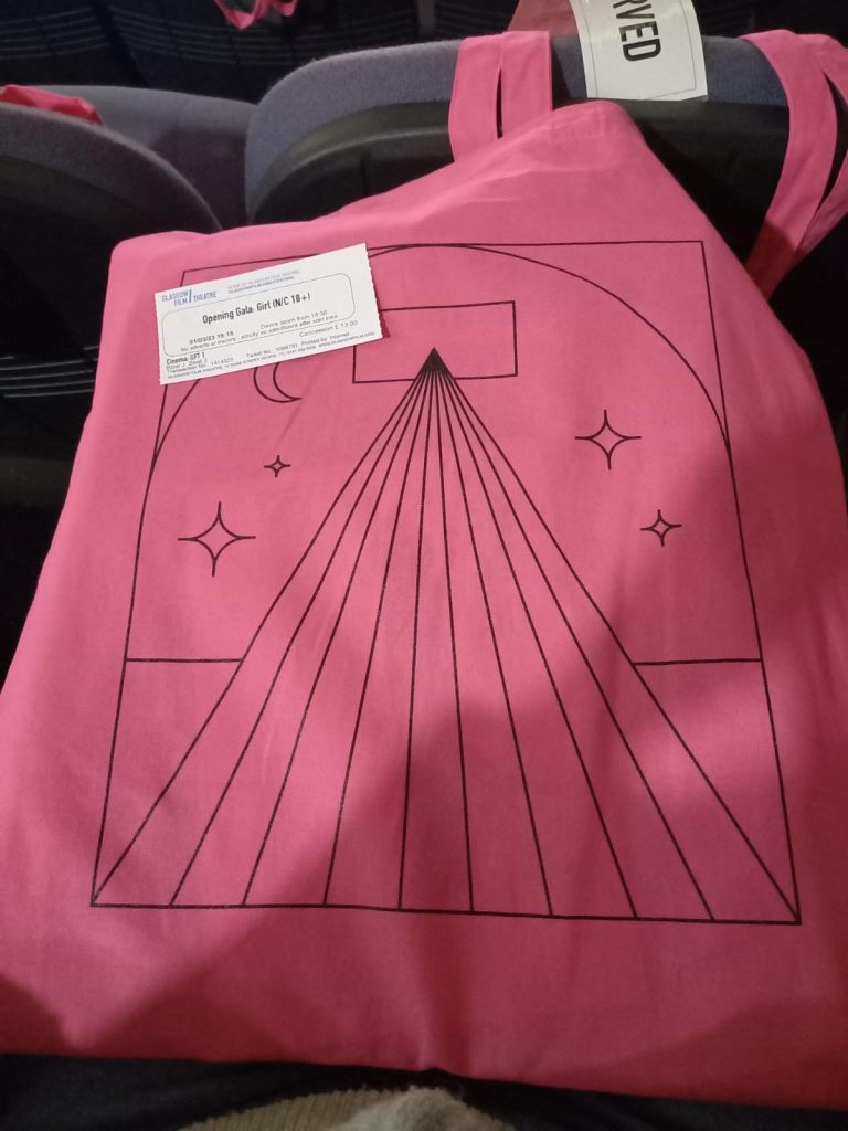 A bright pink tote bag from the festival, looks like the light from a cinema projector is flooding through to create a triangle, with some moon and star shapes dotted around