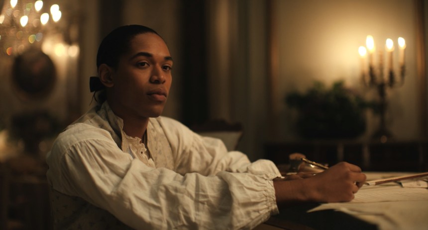 Kelvin Harrison Jr. as Joseph Bologn by candlelight in a white shirt looking thoughtful and composing.