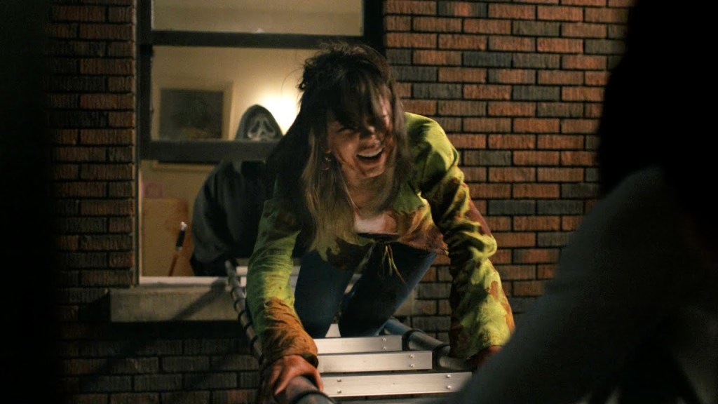 A still of Anika (Devyn Nekoda) in 'Scream VI'. She is seen crawling across a ladder in a bloodstained top screaming in terror while Ghostface watches from the half-open window.