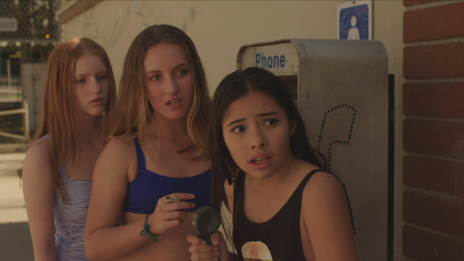The three best friends standing next to a public telephone, Francis is holding the phone away from her ear and they are all looking in the same direction. They are in bathing suits and one of the girls is holding a cigarette.