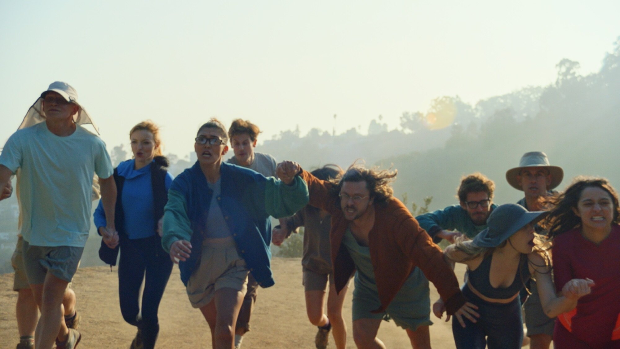 All couples competing in the race shown in motion as they are racing. Every couple is holding hands and they all express various facial expressions ranging from concentration to pure desperation and stress. It looks stressful watching them fight each other for space. 