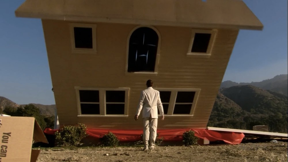 Buster is seen mirroring Buster Keaton in Steamboat Bill, Jr. He is wearing a light-coloured suit and stands with his arms slightly parted from his body as the building is on its way down towards him. 