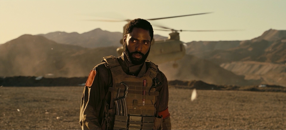 A still from the film 'Tenet' that depicts Protagonist (John David Washington) on a barren landscape. A propeller plane can be seen behind him.