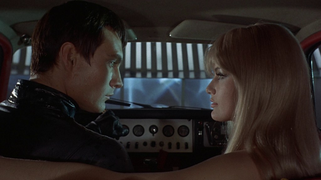 Still from Danger: Diabolik. Close-up. Diabolik and Eva is sitting in a car, with Diabolik in the driver’s seat. They are looking at each other. 
