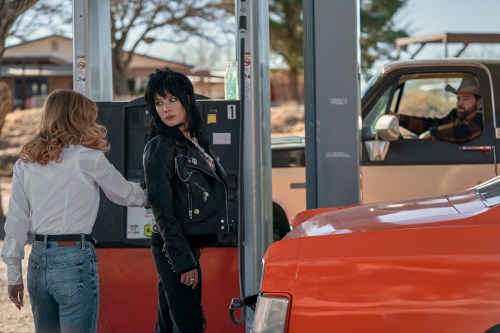 A still of Penny Jo (Sydney Sweeney), Mandy Starr (Halsey), and Lefty (Paul Walter Hauser) in the film 'Americana'. The three of them are at a gas station, with Mandy facing forwards in a leather outfit next to a bright orange car. Lefty is further back in the shot, inside his car.